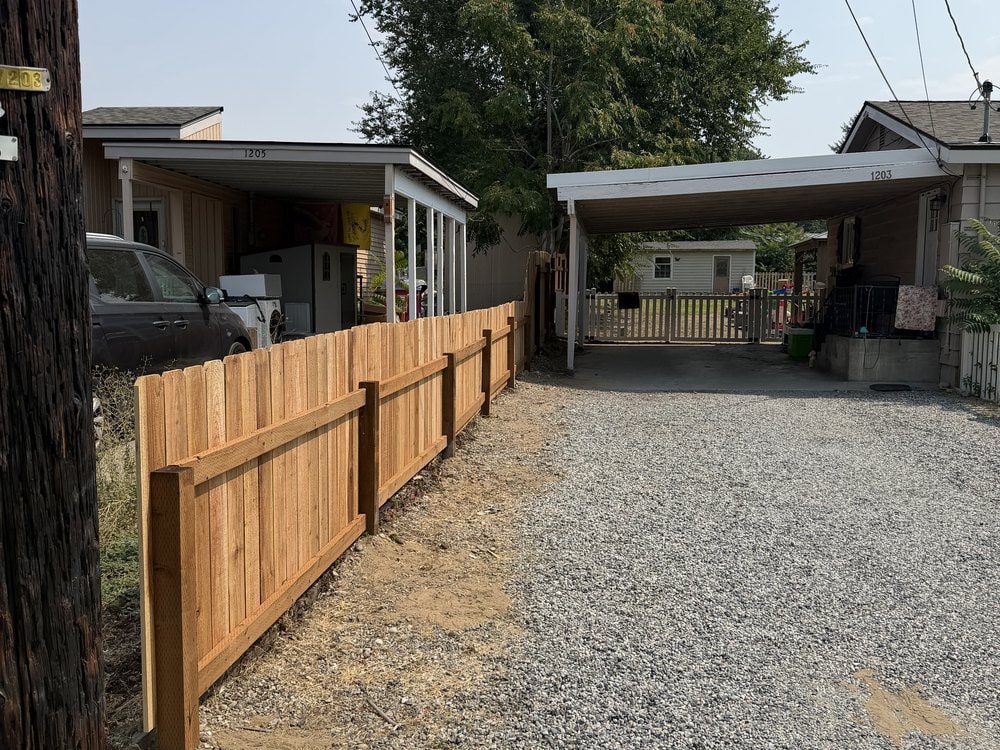 Cedar fence running the length of the gravel drive with bare dirt along its base