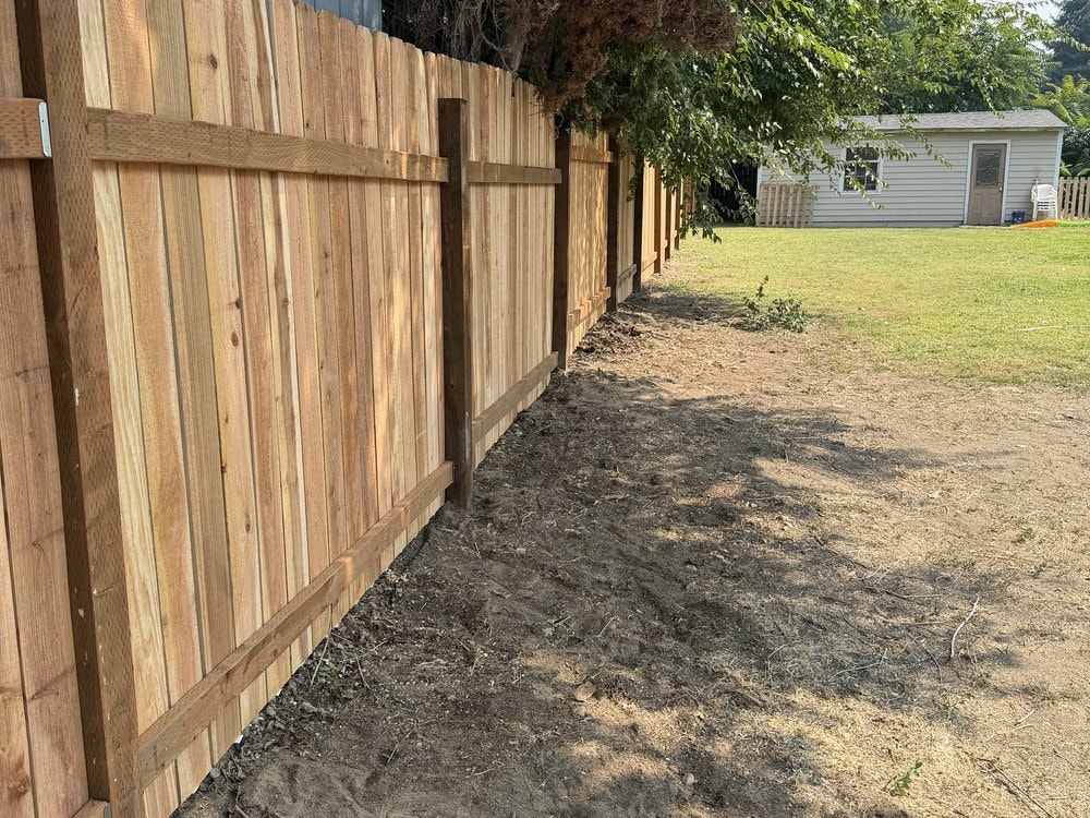 Close view down the back of the cedar fence, rails and posts showing above turned dirt