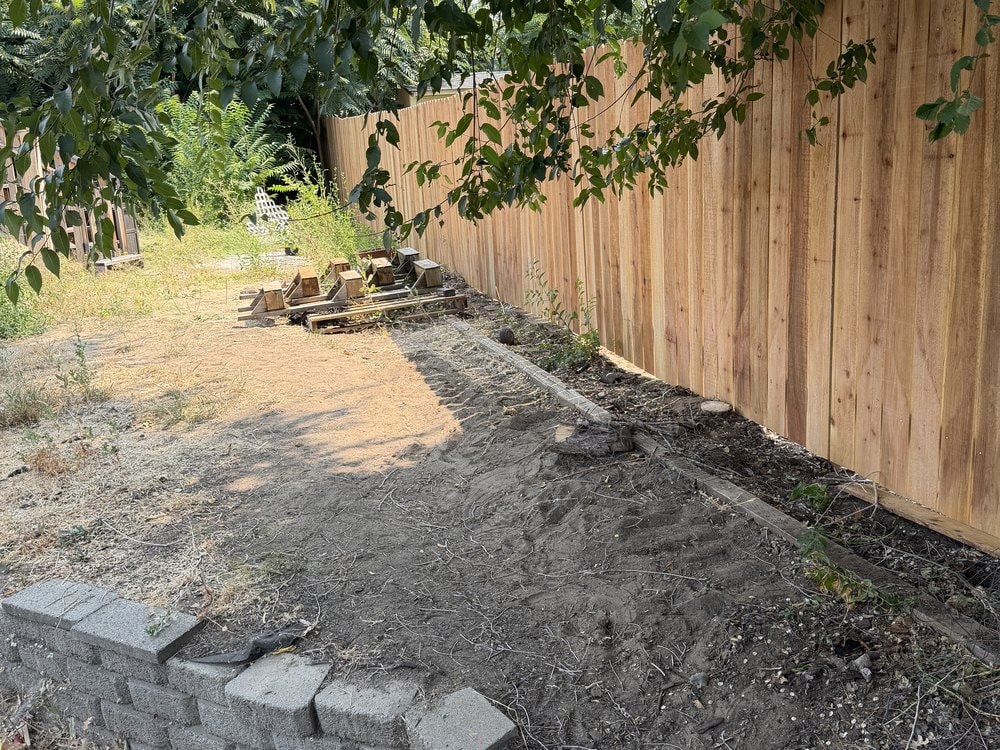 Cedar fence above bare dirt with a low concrete block retaining wall in the foreground