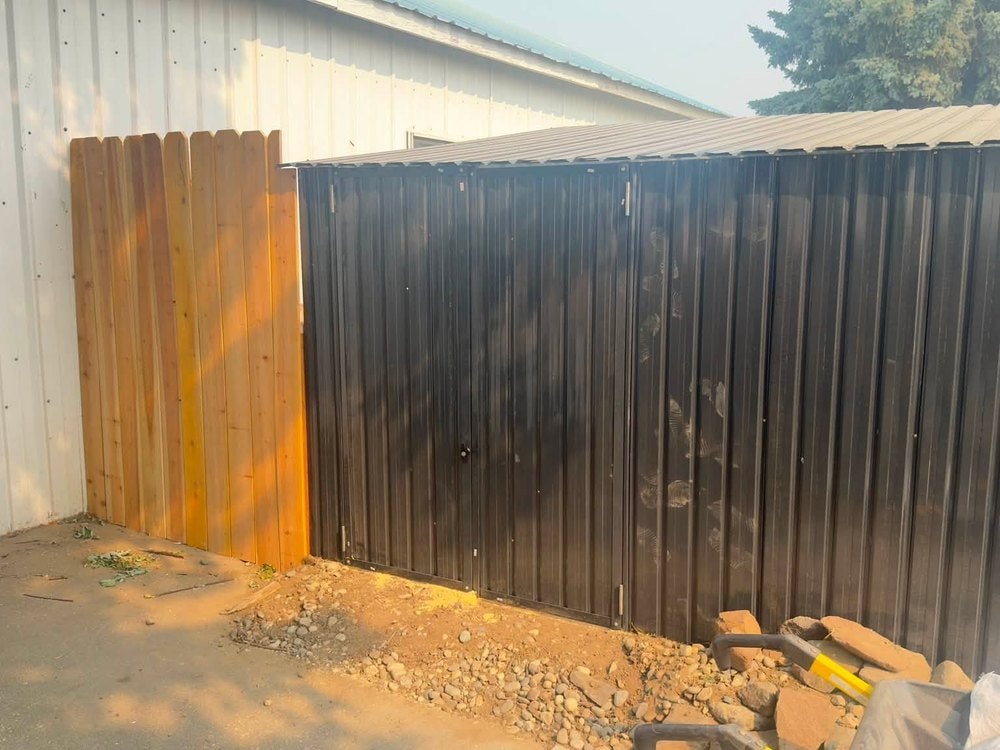 The dark metal shed running along the white shop wall beside a wood fence panel