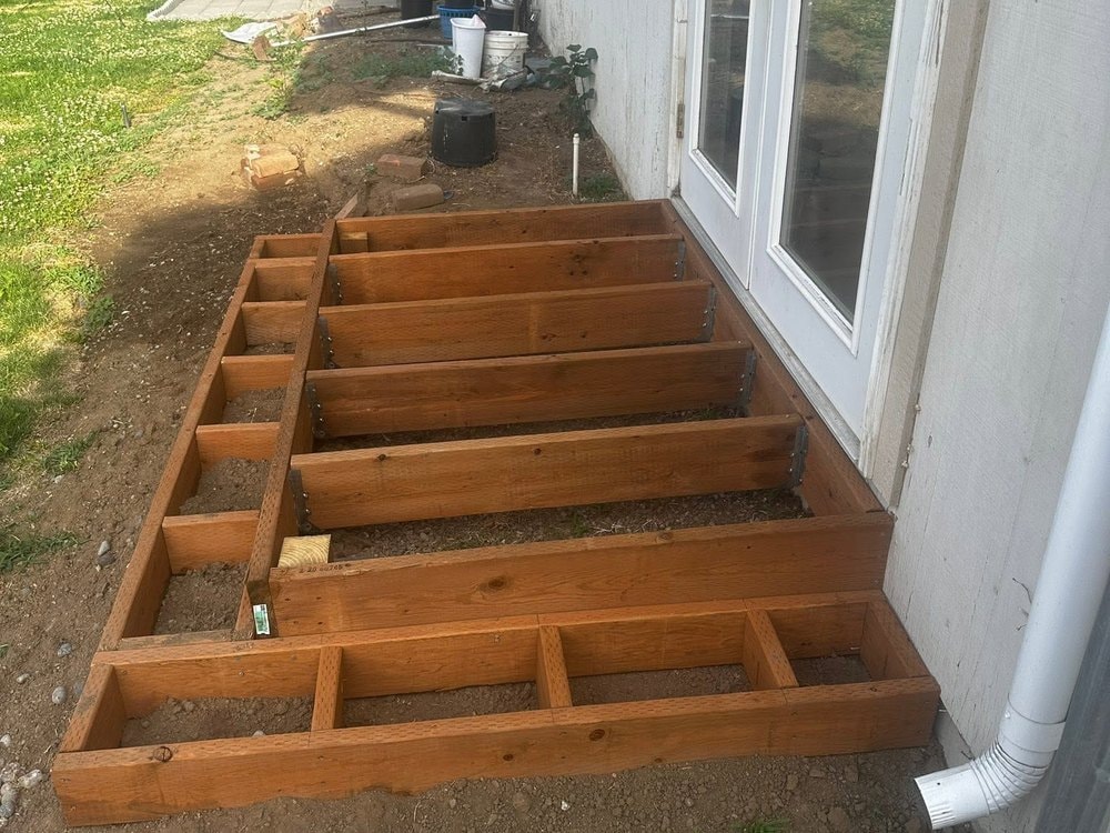 Landing frame set on bare dirt outside a pair of French doors, downspout at right