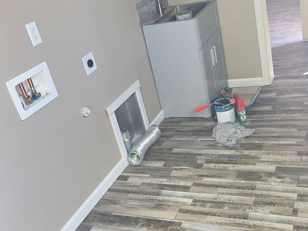 Laundry room with new plank flooring, white baseboard and a grey utility sink, paint supplies still on the floor