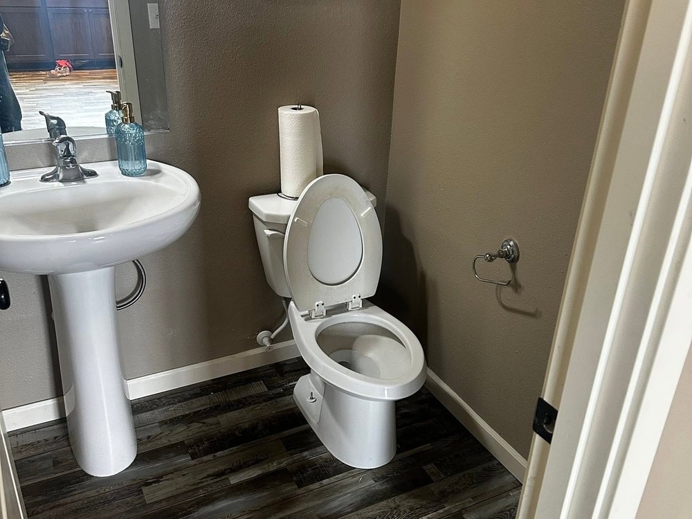 Small bathroom with a pedestal sink, toilet and grey plank flooring running to white baseboard