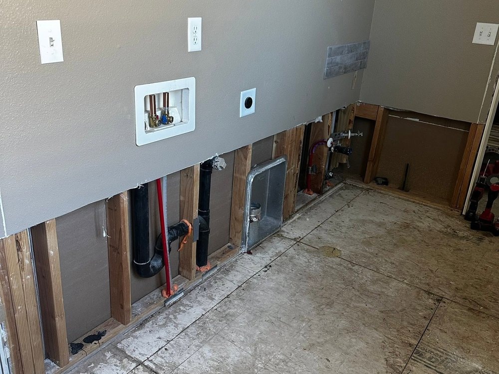 Laundry room wall cut open along the base with exposed studs, drain pipes and bare subfloor