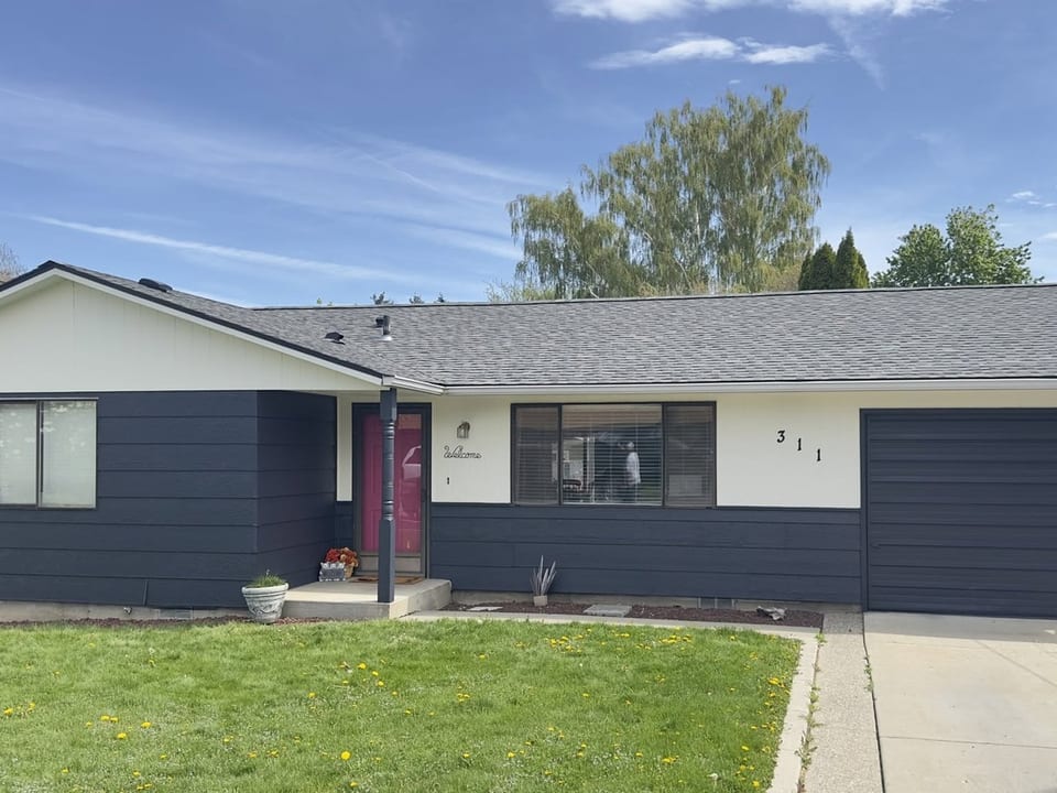 Single story ranch house with dark navy siding, cream upper band, matching navy garage door, and green front lawn.